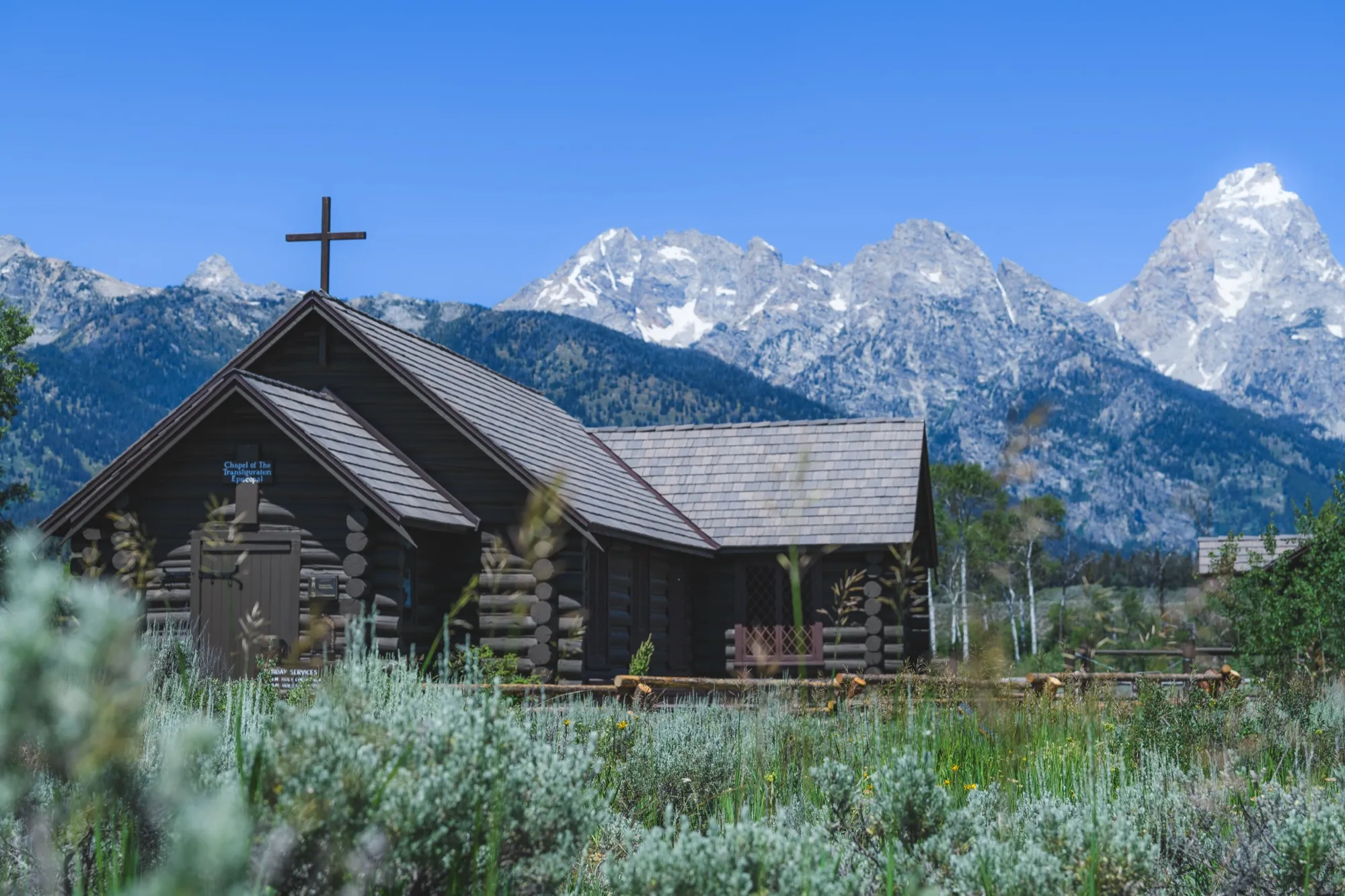 A log chapel with a cross in front of the snow-capped Teton peaks